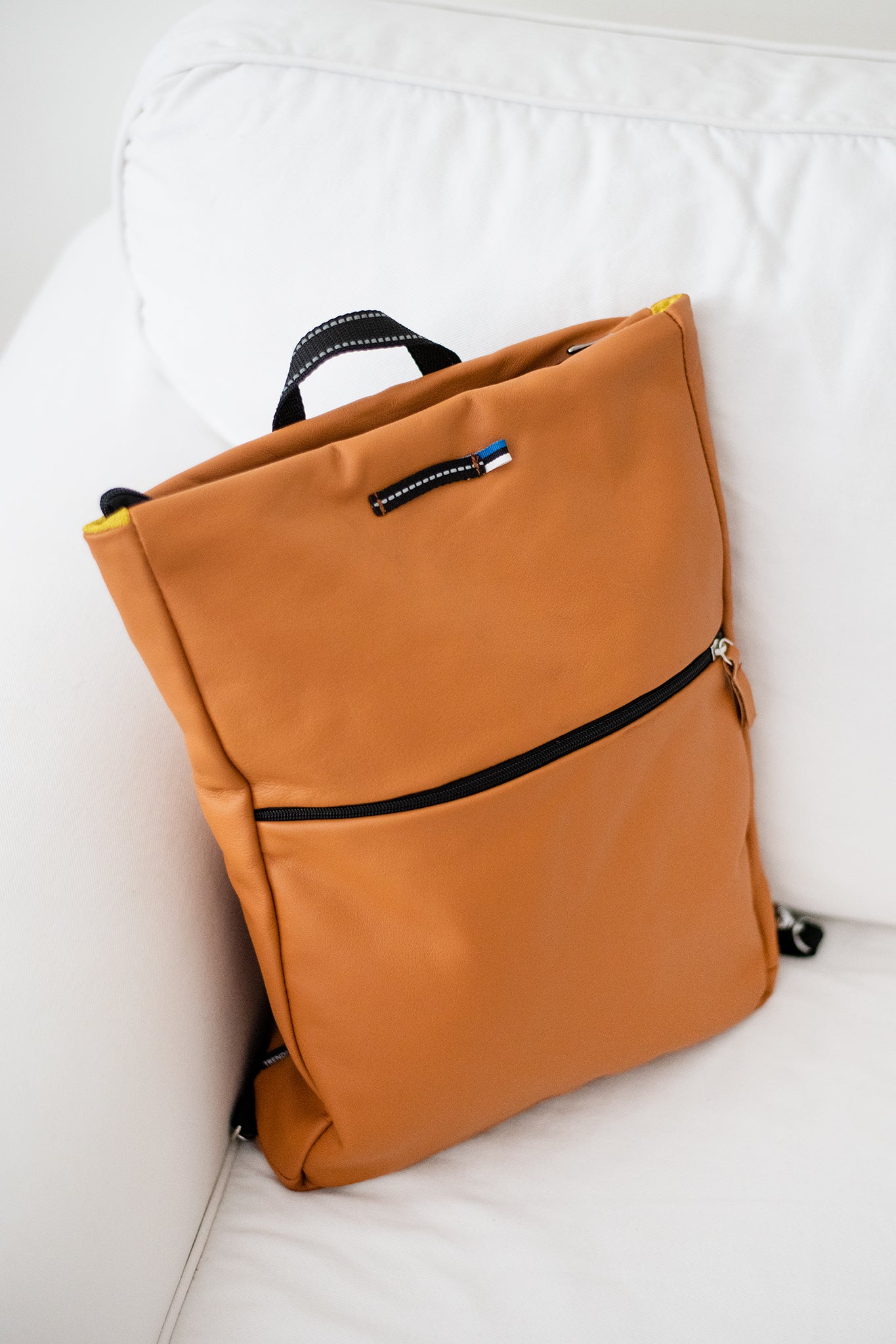 Calvados brown leather backpack with black zipper and handle resting on white couch