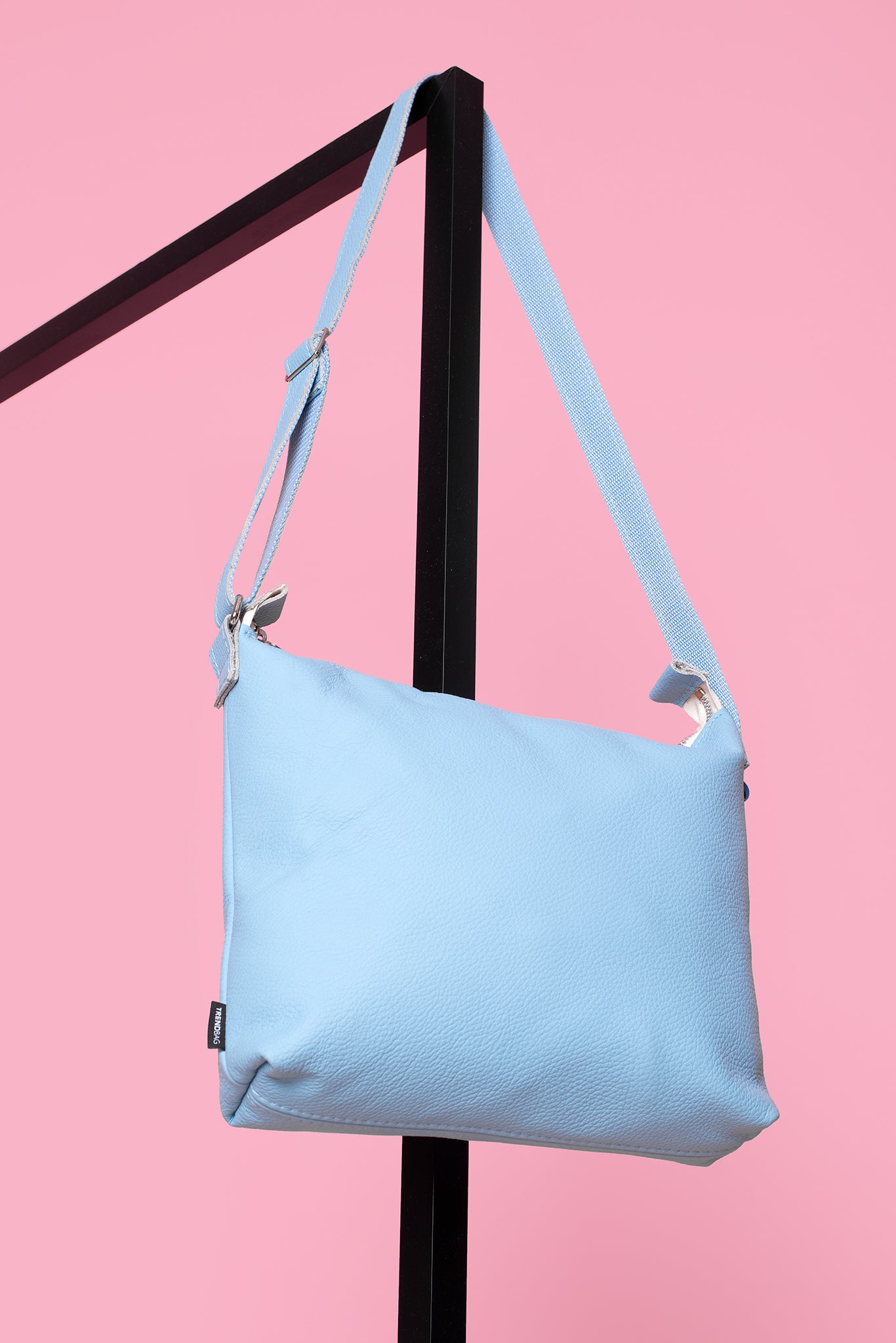 Trendbag light blue shoulder bag with adjustable strap hanging on black stand