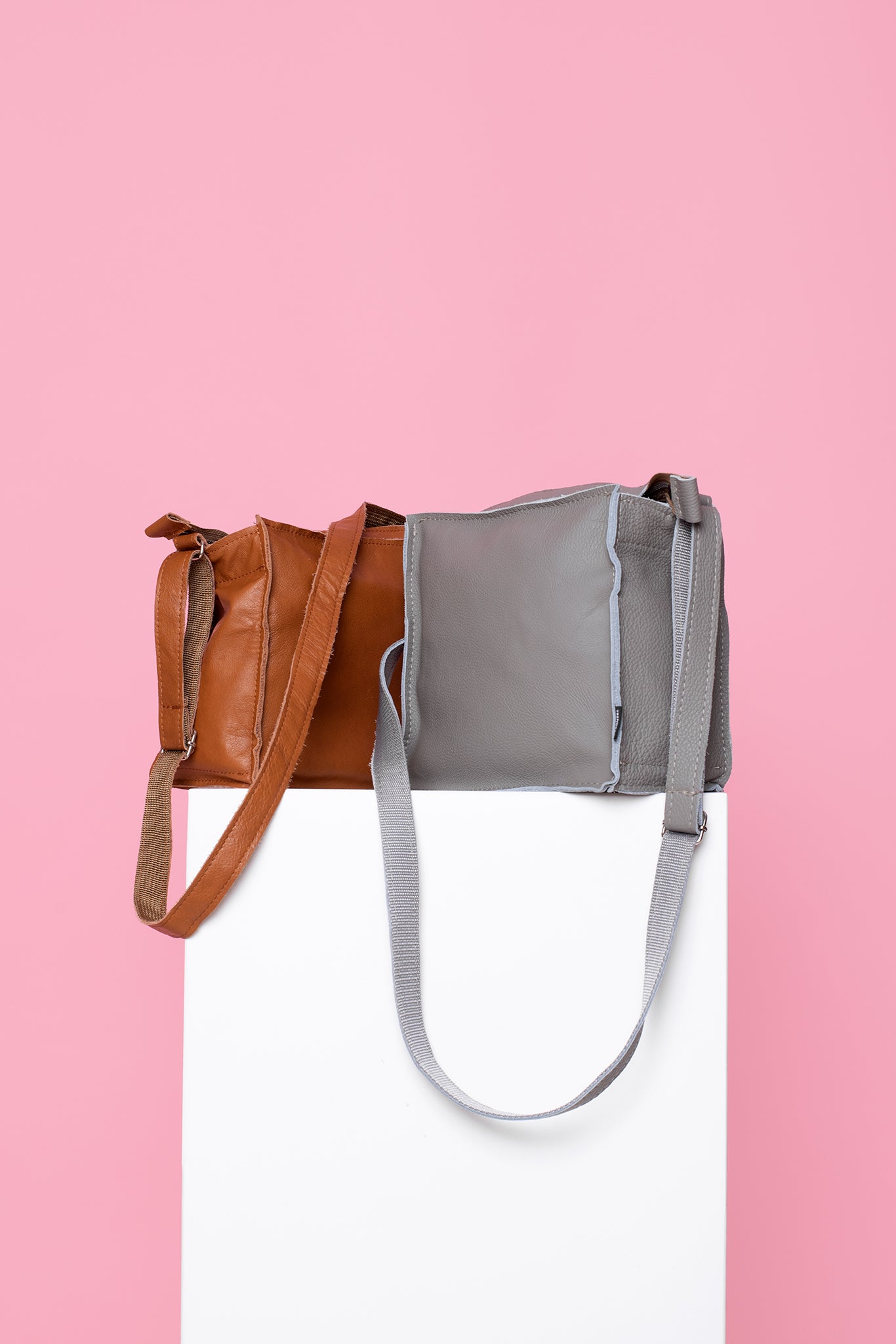 Trendbag light grey shoulder bag displayed alongside a brown bag on a white pedestal with pink background