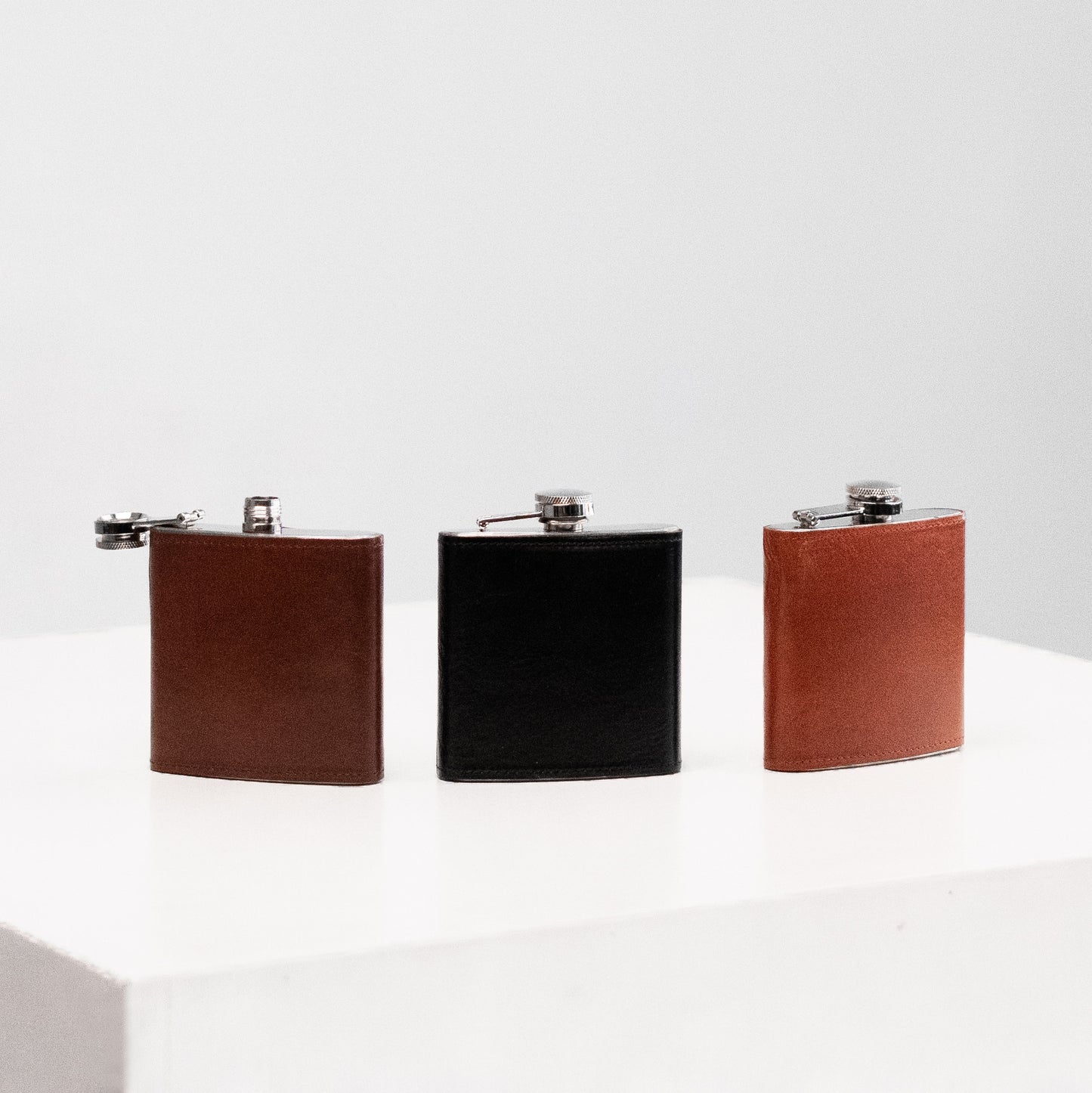 Papillon stylish pocket flask set with brown and black leather covers on a white surface
