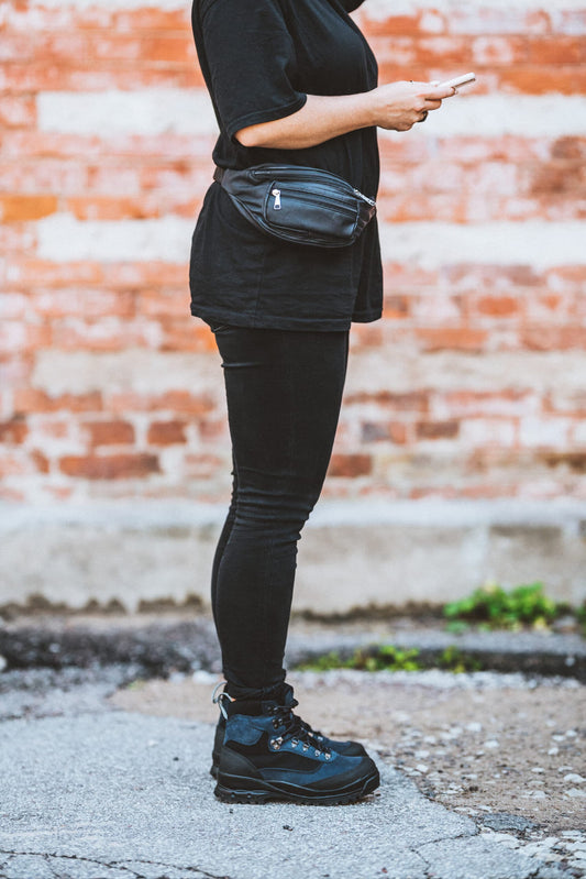 Person wearing a black leather bum bag by Papillon paired with black outfit and sneakers outdoors