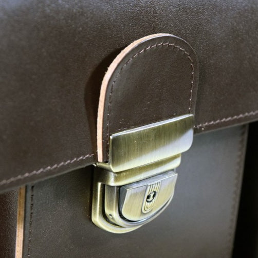 Close-up view of metal clasp on dark brown leather briefcase by Papillon with detailed stitching